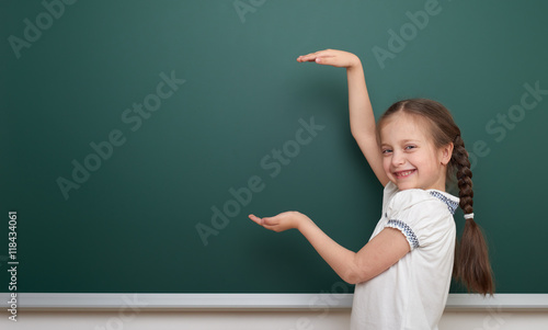 school student girl open arms at the clean blackboard, grimacing and emotions, dressed in a black suit, education concept, studio photo