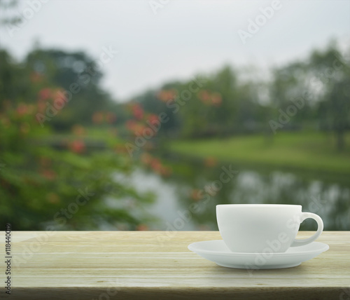 White coffee cup on wooden table over blur of red flower and tre