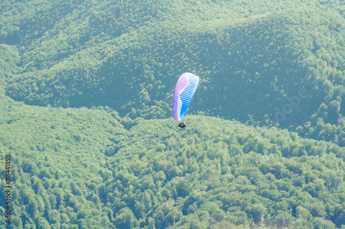 Paraglider in the sky over the green hills