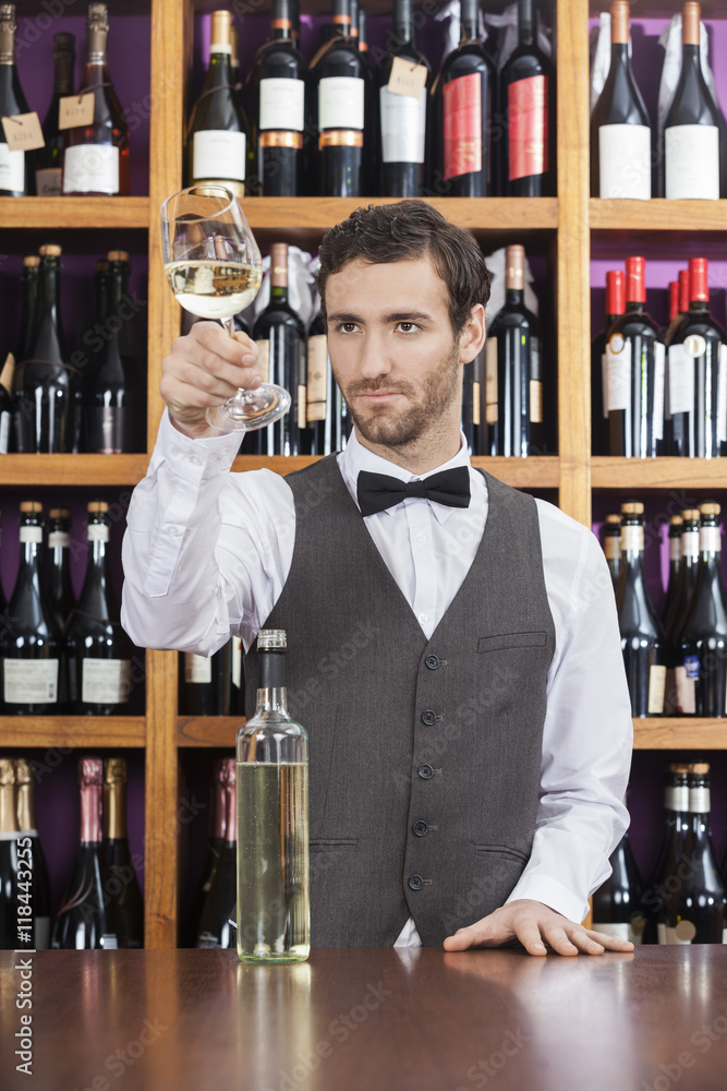 Bartender Examining White Wine In Glass At Shop Counter Bartender Examining White Wine In Glass At Shop Counter