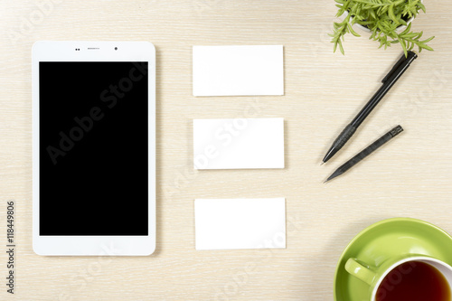 Business card blank, smartphone or tablet pc, flower, coffee cup and pencil at office desk table top view. Corporate stationery branding mock-up