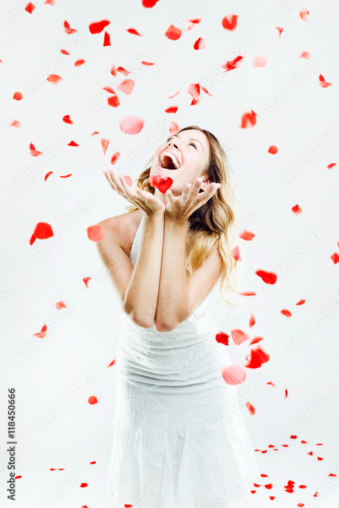 Beautiful young woman under a rain of rose petals. Isolated on w