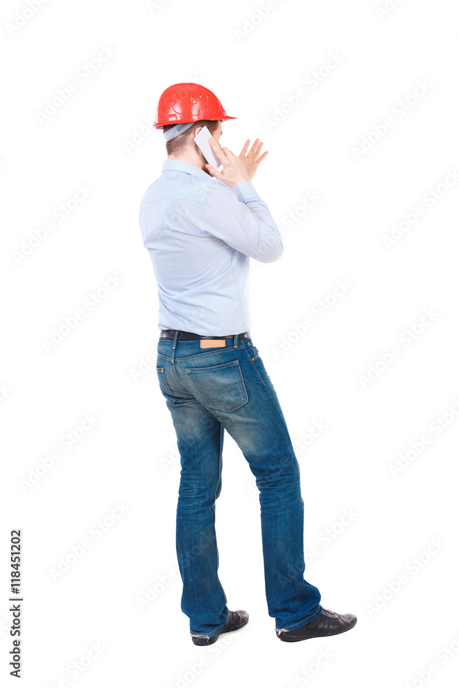 Backview of business man in construction helmet stands and enjoys tablet or using a mobile phone. Standing young guy. Rear view people collection. backside view of person. Isolated over white Backview of business man in construction helmet stands and enjoys tablet or using a mobile phone. Standing young guy. Rear view people collection. backside view of person. Isolated over white