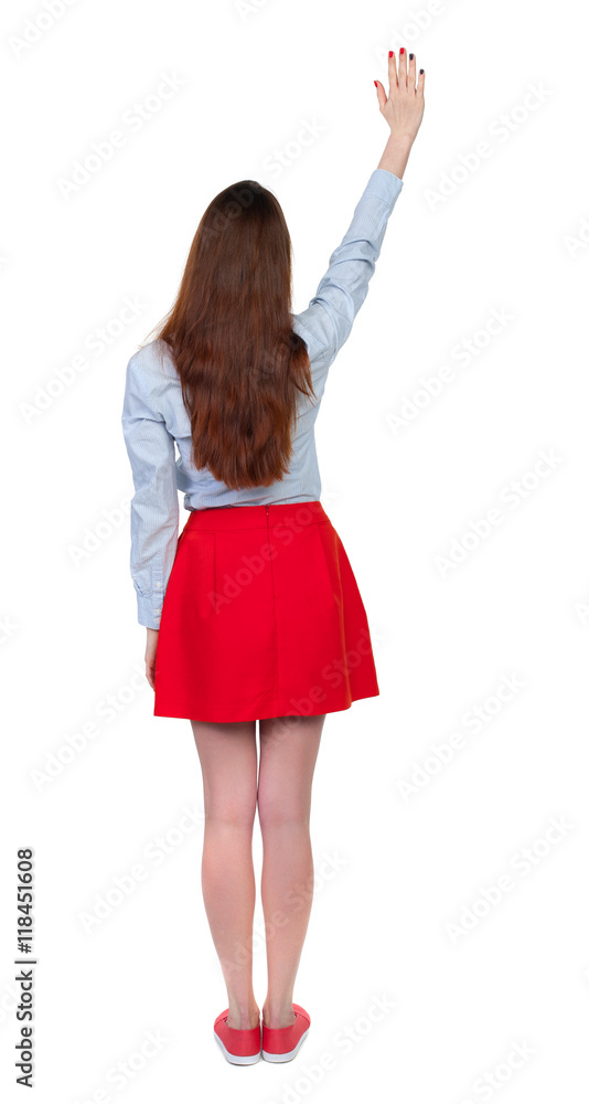 Fototapeta premium Back view of beautiful woman welcomes. Young teenager girl hand waving from. Rear view people collection. backside view of person. Isolated over white background. Long-haired brunette in red skirt