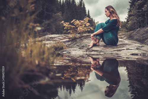 Beautiful woman posing near pond with mountain forest on the background.