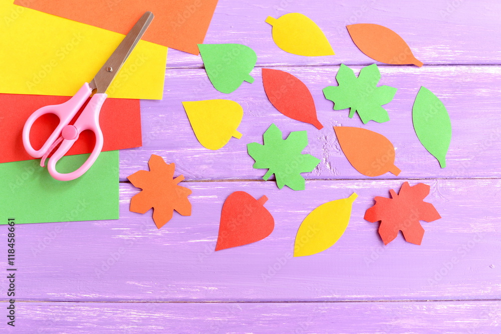 Cut yellow, green, red and orange paper leaves, scissors, colored paper  sheets on lilac wooden background. Easy autumn crafts for kids in  kindergarten at home. Closeup Stock Photo
