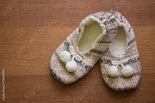 Knitted slippers with pompoms on wood floor. 