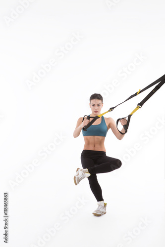 Upper body excercise concept. Picture of beautiful fitness trainer or coach showing her strong body with muscles. Pretty lady training with suspension trainer sling isolated on white background.