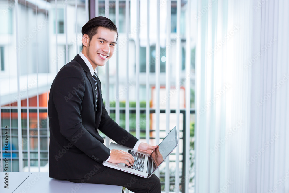 Portrait Of A Handsome Young Happy Man Using laptop in office Portrait Of A Handsome Young Happy Man Using laptop in office