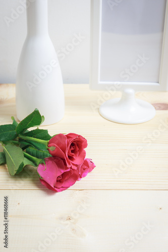 White vase, frame of photography and pink roses on the wood floor.