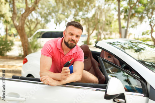 Young bearded man standing near convertible with keys in hand