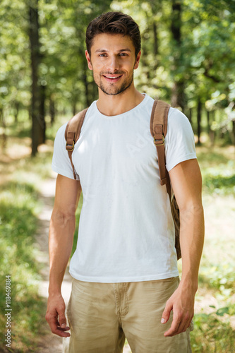 Cheerful young man with backpack standing in forest