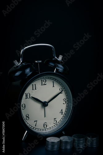 saving time, Alarm clock standing with coins isolated on black background. with vintage filter