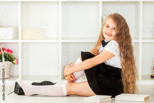 Canvas Print smiling little schoolgirl in school uniform sitting near bookshe