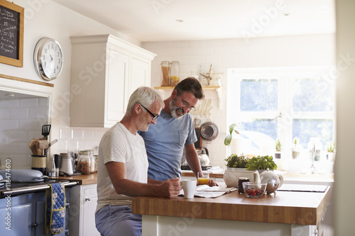 Male couple in their kitchen reading a paper in the morning photo