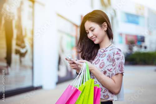 Happy young woman using cell phone at a shopping center,high key