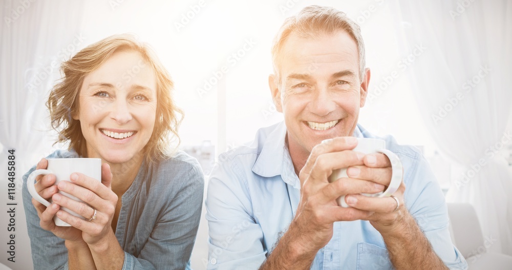 Smiling middle aged couple sitting on the couch having coffee - obrazy, fototapety, plakaty 