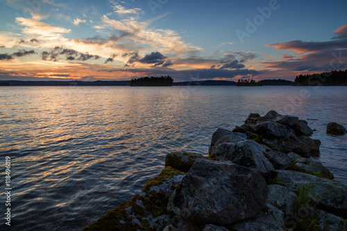 View of an old and broken pier made of rocks and lake at sunset in Finland in the summer.