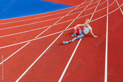 Athletic female runner rests on running track at sports arena