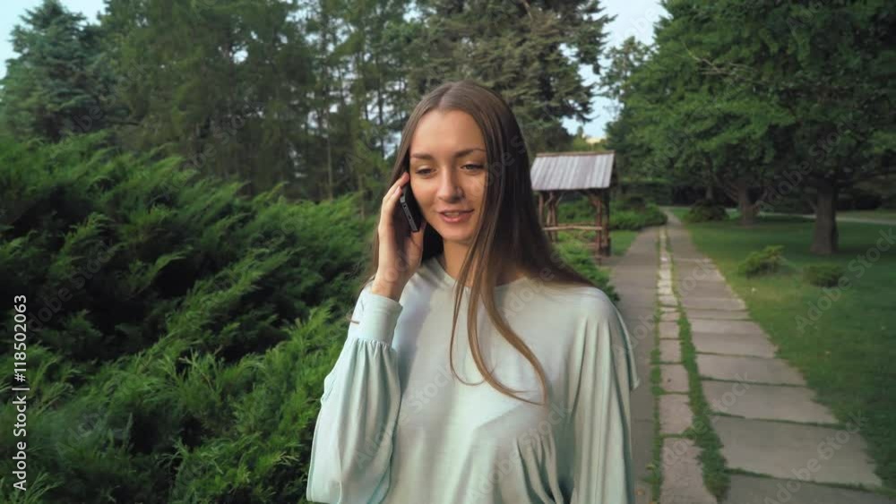Young attractive girl with long hair walking on a path in the park and talking on the phone. Young attractive girl with long hair walking on a path in the park and talking on the phone.