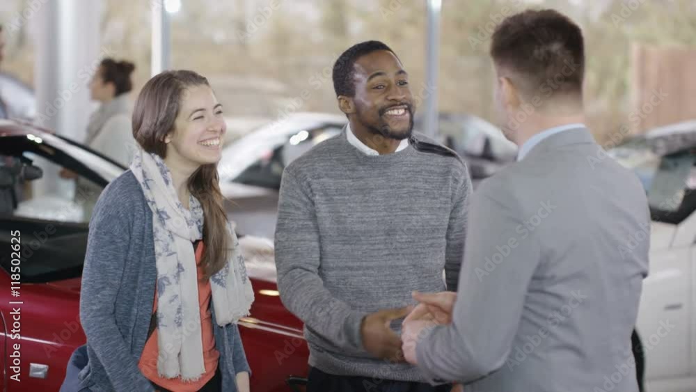 Happy couple in car dealers shake hands with salesman & take key to new car Happy couple in car dealers shake hands with salesman & take key to new car