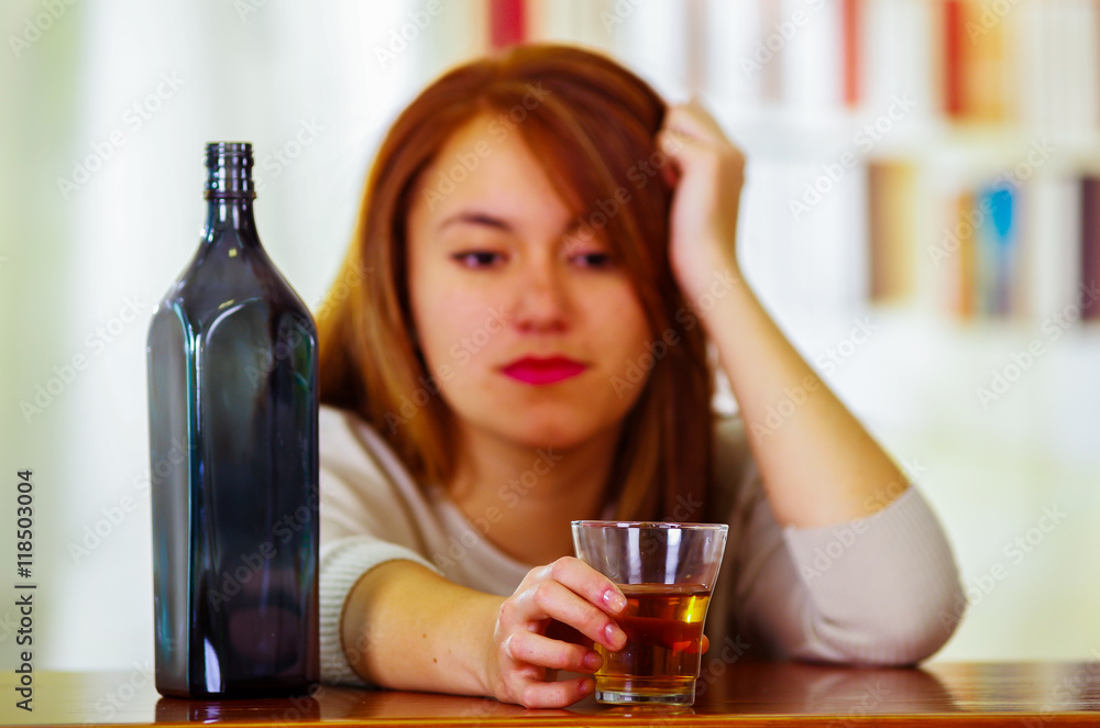 Attractive woman wearing white sweater sitting by bar counter lying over desk next to glass and bottle, drunk depressed facial expression, alcoholic concept Attractive woman wearing white sweater sitting by bar counter lying over desk next to glass and bottle, drunk depressed facial expression, alcoholic concept