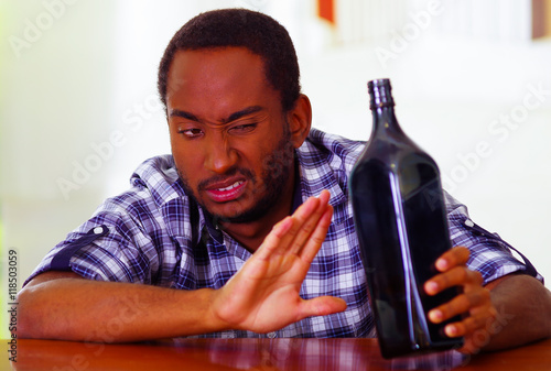 Handsome man wearing white blue shirt sitting by bar counter lying over desk expressing no desire to keep drinking using body language, drunk depressed facial expression, alcoholic concept