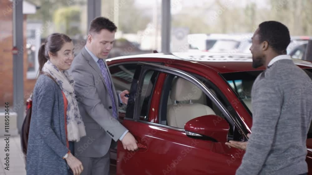 Excited couple in car dealership take key to new car from salesman Excited couple in car dealership take key to new car from salesman