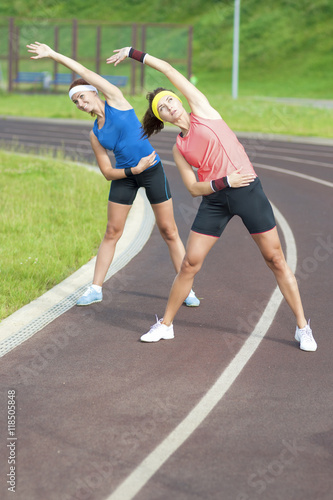 Portrait of Two Young Feale Sportswomen Having Stretching Exercises At Sport Venue Outdoors