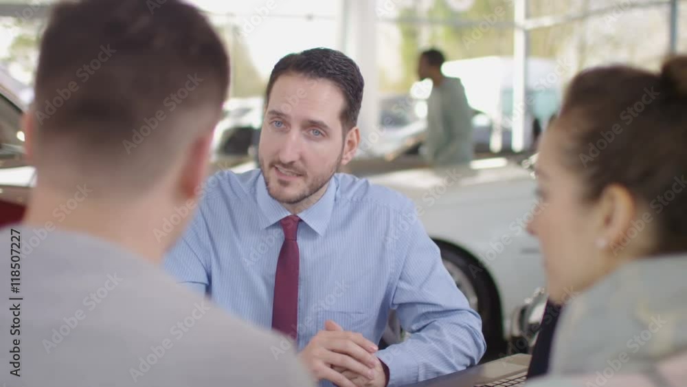 Happy couple in car dealers shake hands with salesman & take key to new car Happy couple in car dealers shake hands with salesman & take key to new car