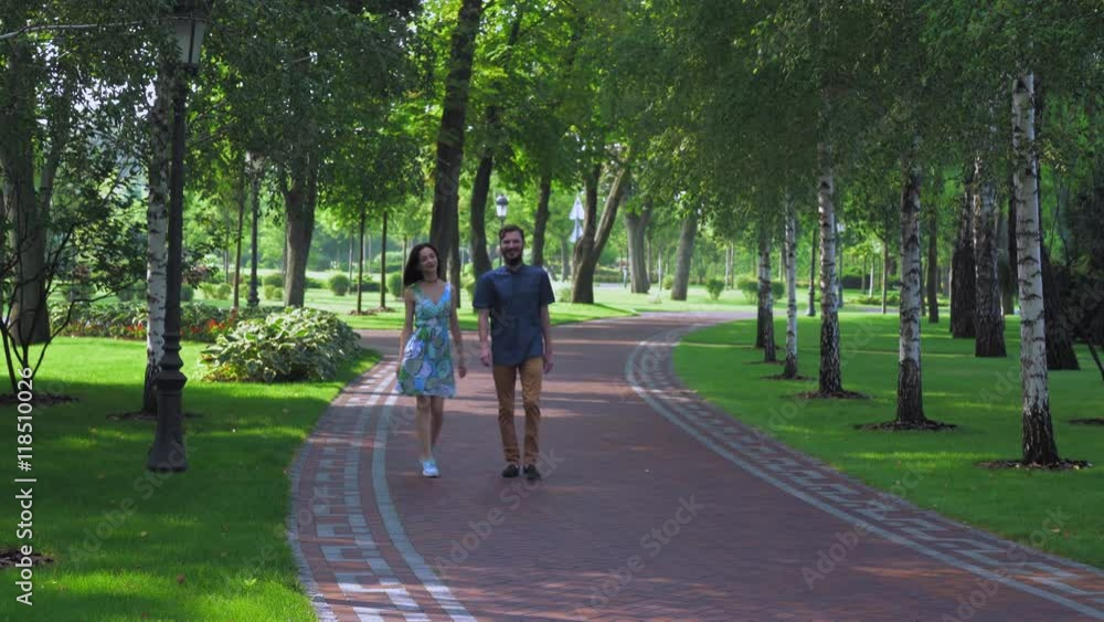 Young couple walking on a path of tiles in a summer park with birches. They smile and talk. Young couple walking on a path of tiles in a summer park with birches. They smile and talk.