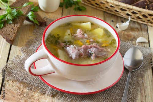 Delicious soup with rice and chunks of meat, rye bread on a wood photo