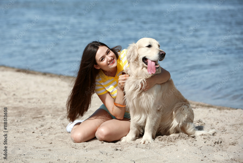 Beautiful girl with cute retriever on river shore
