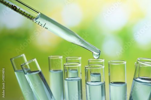 Fotografía Close up of a pipette dropping a  sample into a test tube on light green backgro