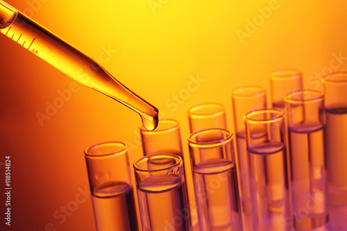 Close up of a pipette dropping a  sample into a test tube on colourful background