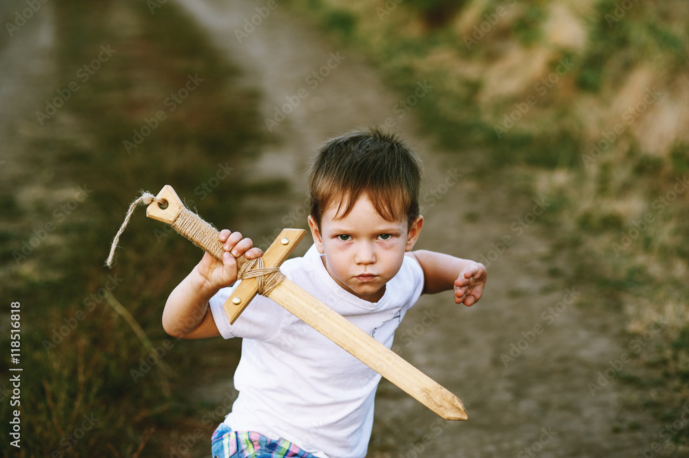 a boy plays with a wooden sword , on a dirt road .