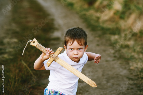Obraz na płótnie a boy plays with a wooden sword , on a dirt road . w salonie
