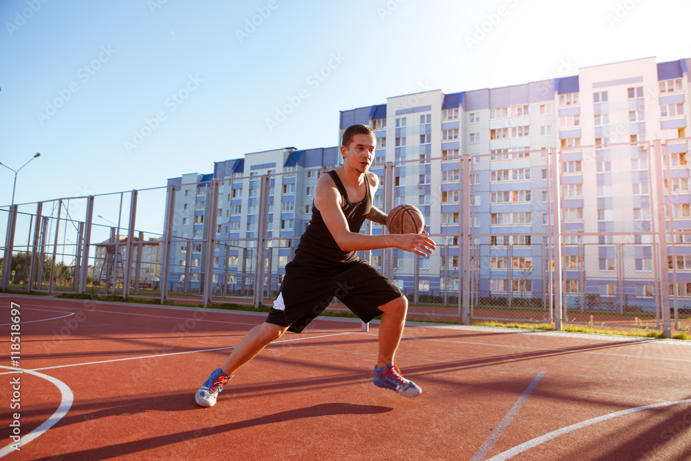 One guy play basketball at district sports ground against a backdrop residential buildings.