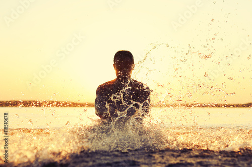 Strong man splashing in the water at sunset
