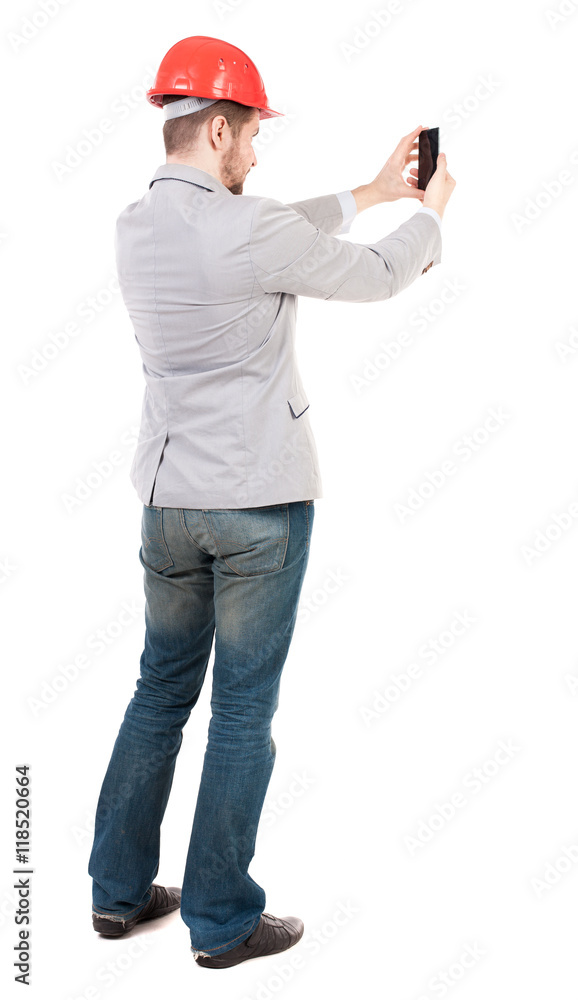 Backview of business man in construction helmet stands and enjoys tablet or using a mobile phone. Standing young guy. Rear view people collection. backside view of person. Isolated over white Backview of business man in construction helmet stands and enjoys tablet or using a mobile phone. Standing young guy. Rear view people collection. backside view of person. Isolated over white