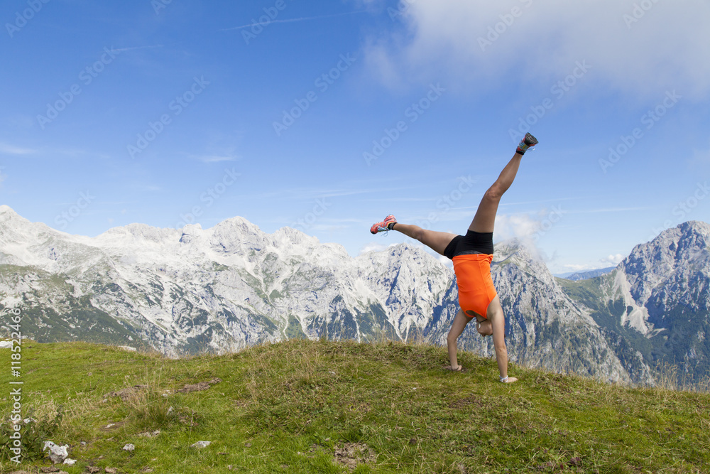 Young pretty women joyfully jumping and performing cartwheel, outdoors high in the mountains, on sunny summer day