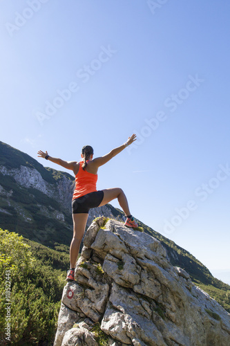 Young pretty smiling woman hiker standing on a rock with raised outstretched hands, high in the mountains, freedom and happiness, achievement in mountains 