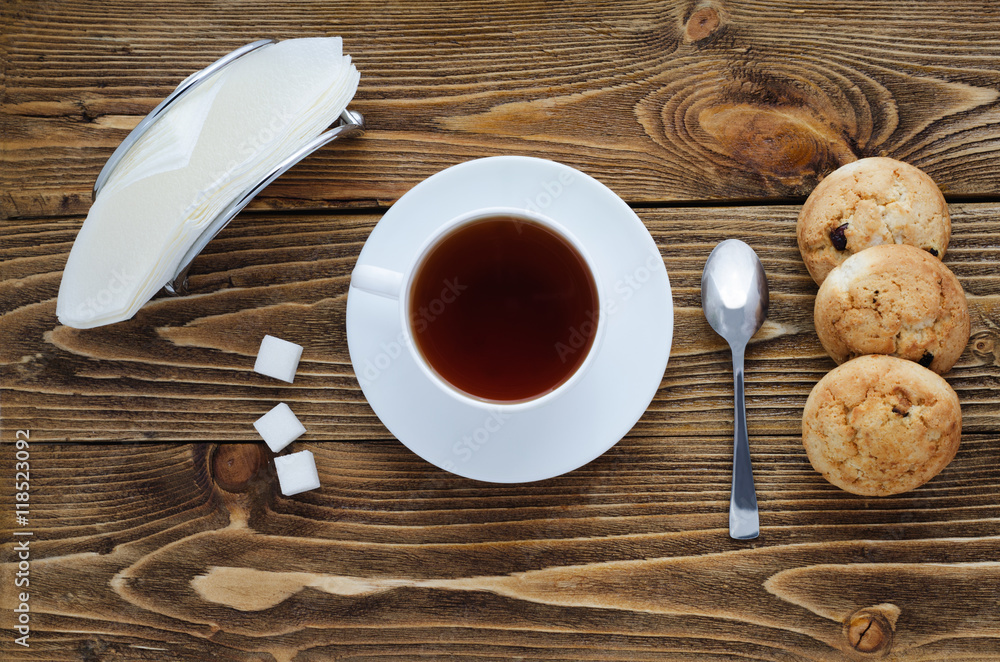Obraz premium Cup of tea on a wooden table, sugar, spoon, biscuits, napkins, top view