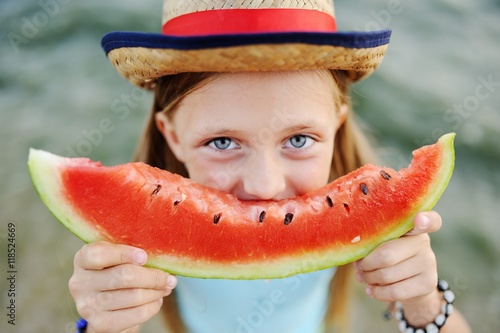 baby girl in the hat eagerly eats juicy watermelon on sea background