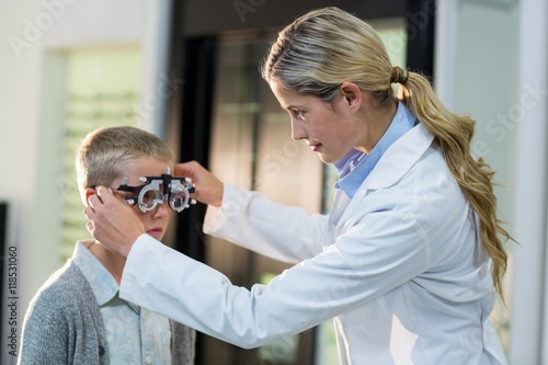 Female optometrist examining young patient with phoropter