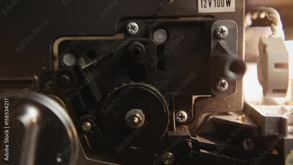 Inside a super 8mm film projector: a spinning wheel, the lamp, the on-off button. A hand turns off the machine. Macro detail angled shot.
Inside a super 8mm film projector: a spinning wheel, the lamp, the on-off button. A hand turns off the machine. Macro detail angled shot.