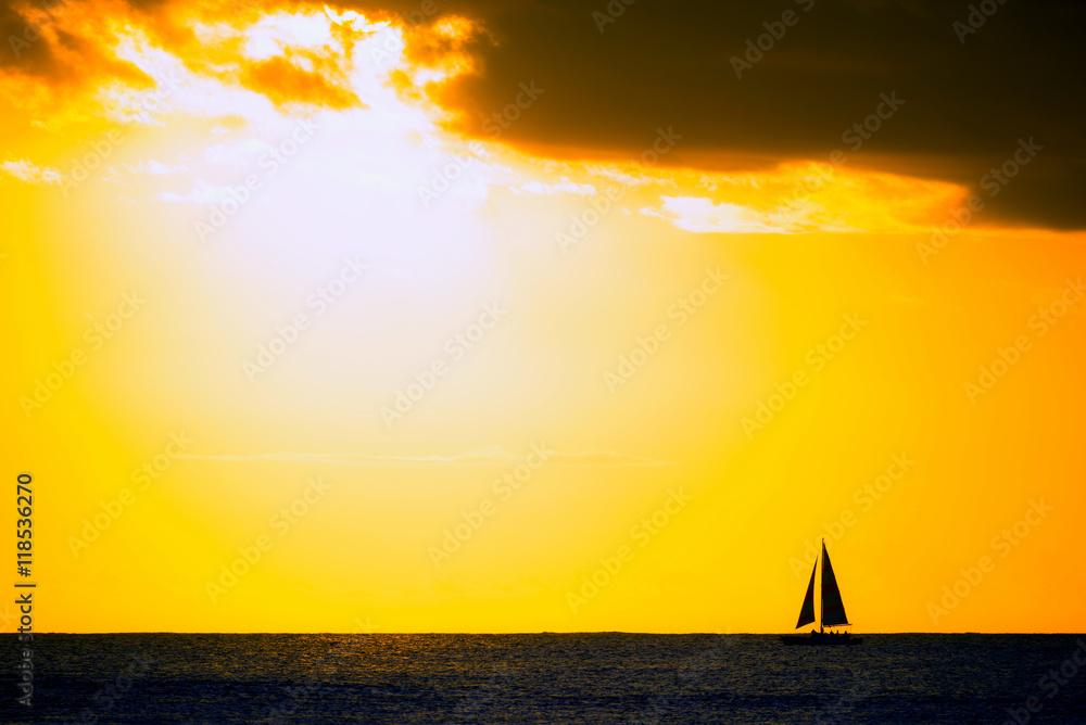 Fototapeta premium Silhouette of sailboat on horizon under partially cloudy skies at sunset