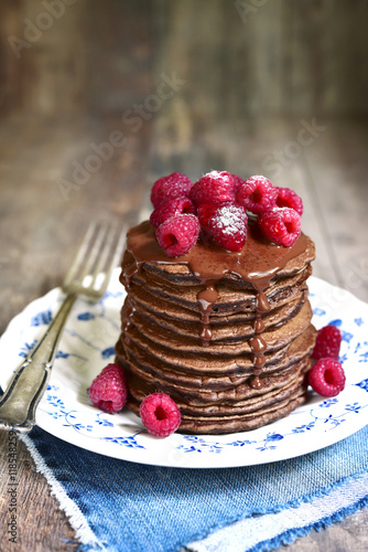 Stack of chocolate pancakes topped with chocolate and fresh rasp