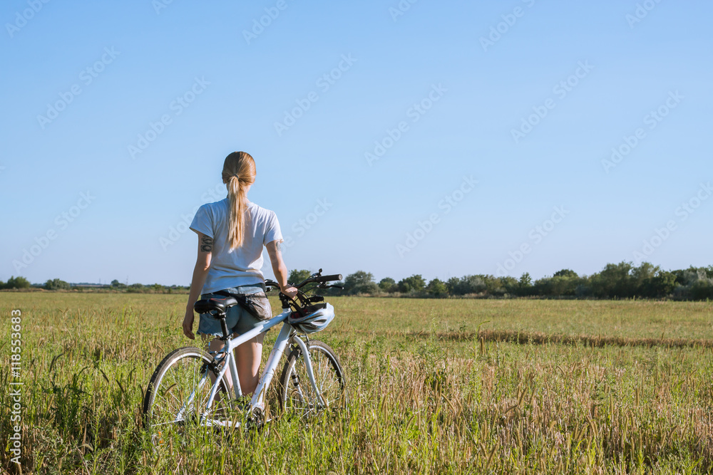 Obraz premium young woman with bicycle walking in fields 