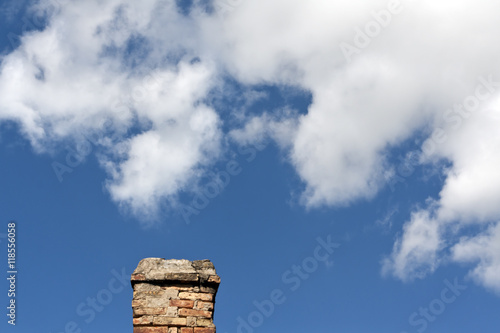 Old brick chimnet against blue sky with clouds.